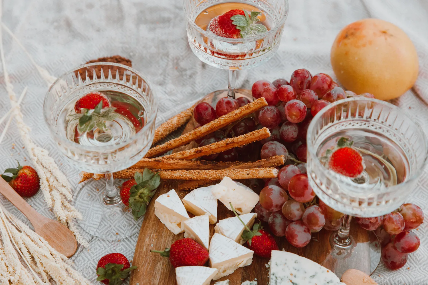 Une planche de fromages, de raisin, de fraises et de gressins, et trois coupes posées sur un plaid, EVJF à Bordeaux
