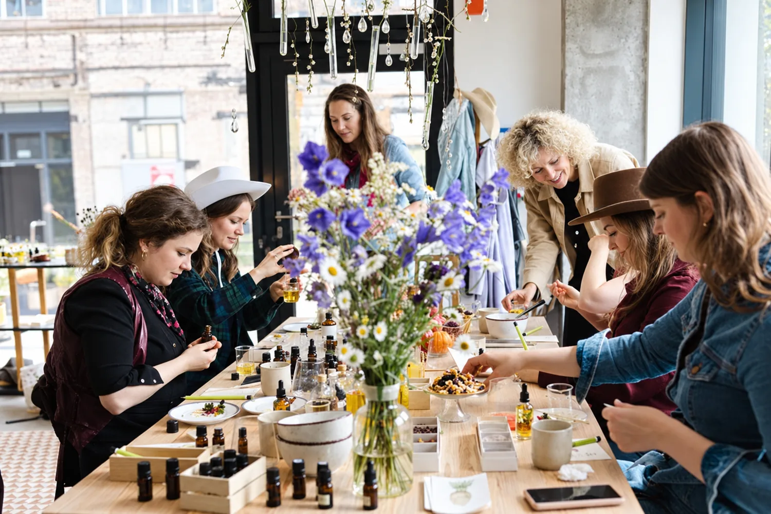 Une grande tablée d'atelier cosmétique : flacons compte-gouttes, bols, fleurs, chacune à sa préparation, EVJF à Bordeaux
